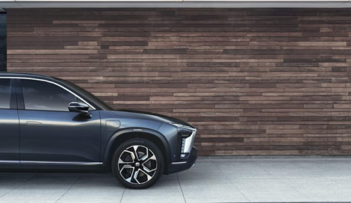 Photo of car parked in front of wall made of wood bars.