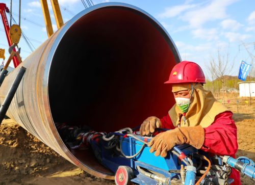 a construction worker in front of a massive pipe works on installing it