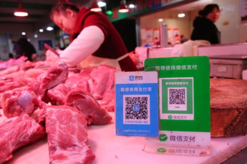 a meat market in beijing, with qr codes for two payment platforms, wechat pay and alipay, displayed in the foreground to the right