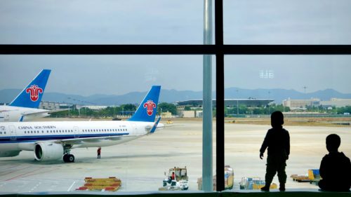 A young boy watches two Chinese airliners from the airport terminal, as his father looks on.