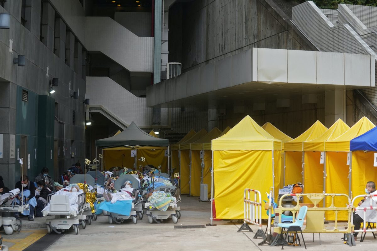 COVID patients wearing face masks lie in bed at an area outside a hospital in Hong Kong with yellow tents